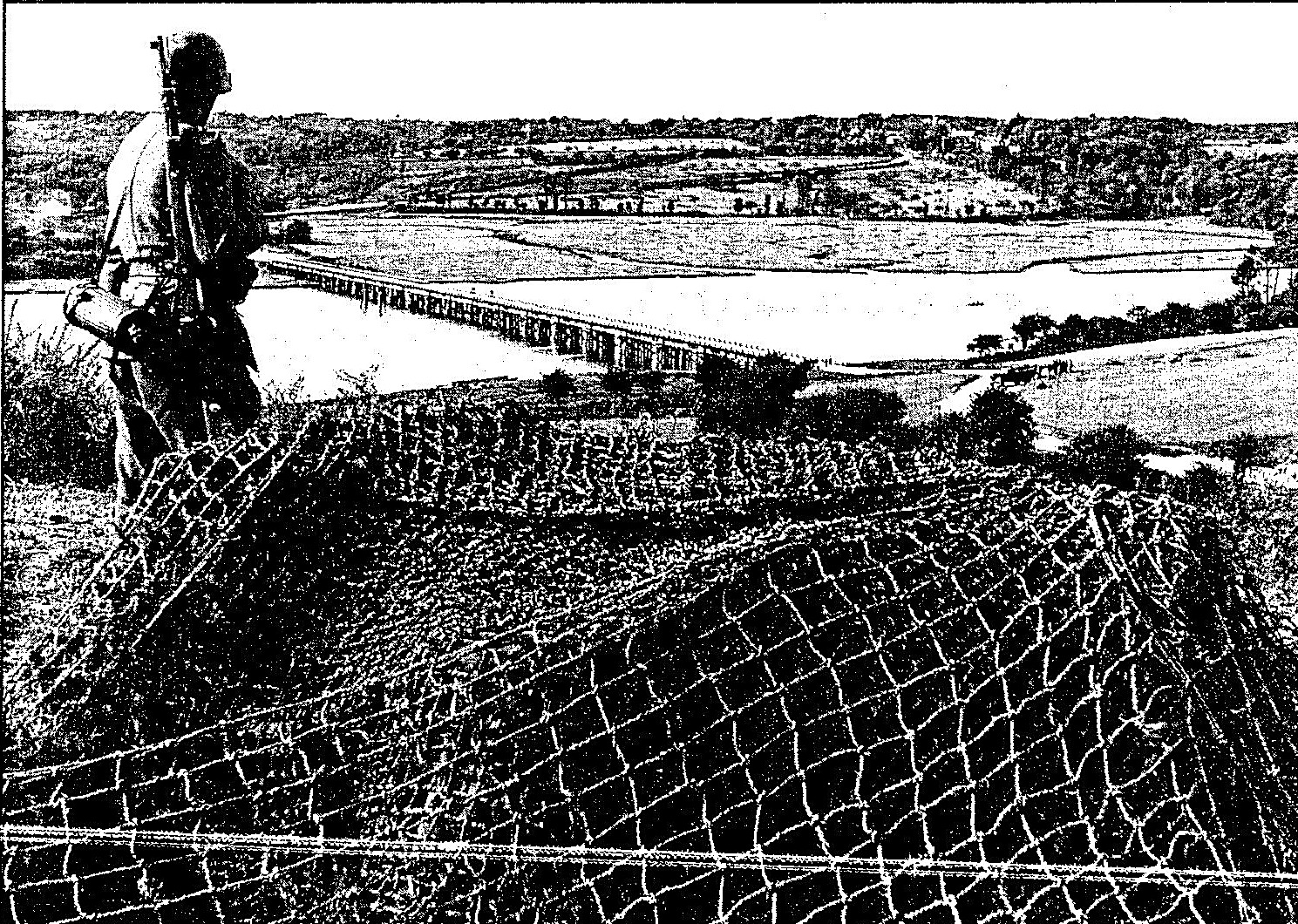 Soldat allemand montant la garde près d’une batterie camouflée dominant le pont de bois encore intact.